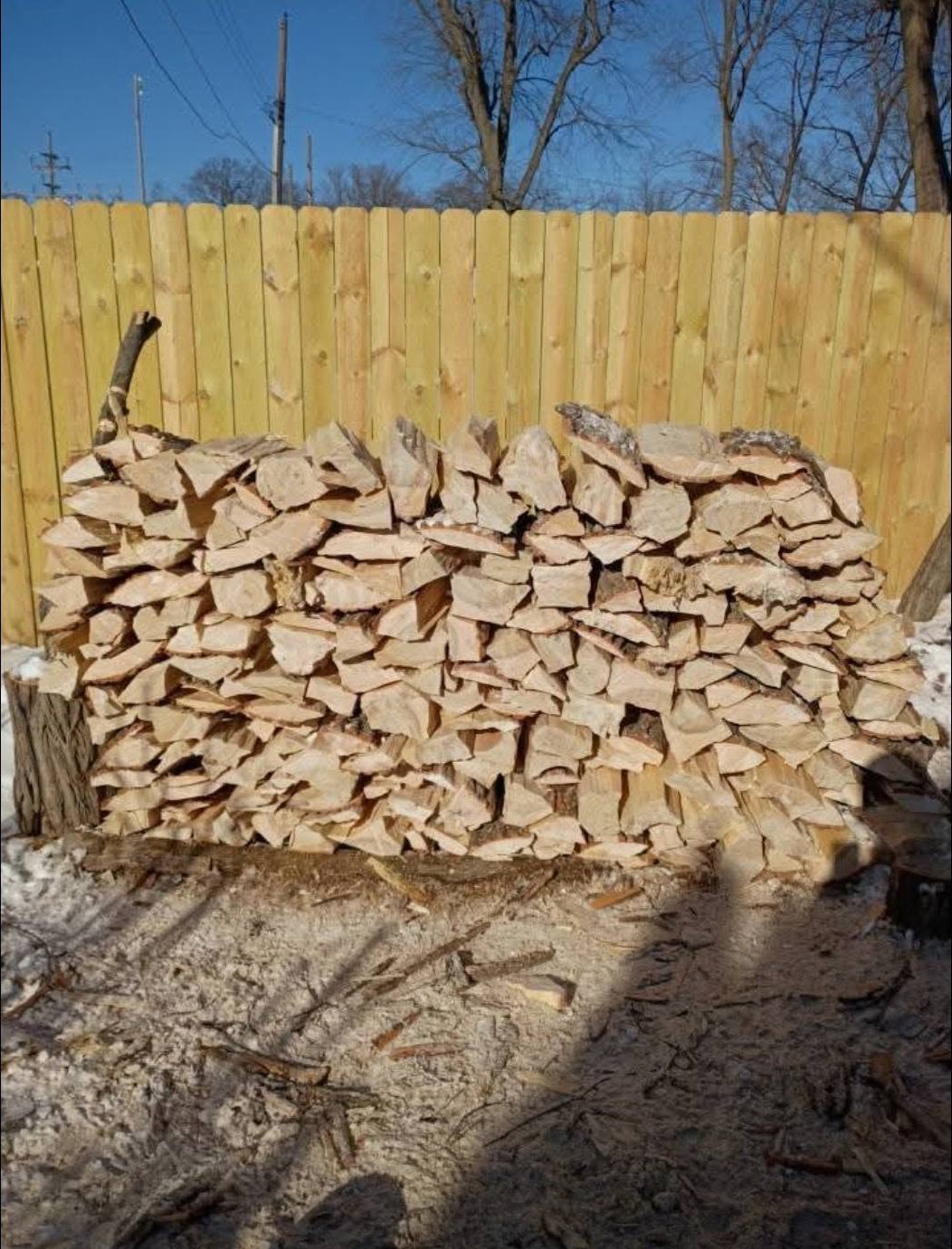A face cord of split firewood stacked against a fence